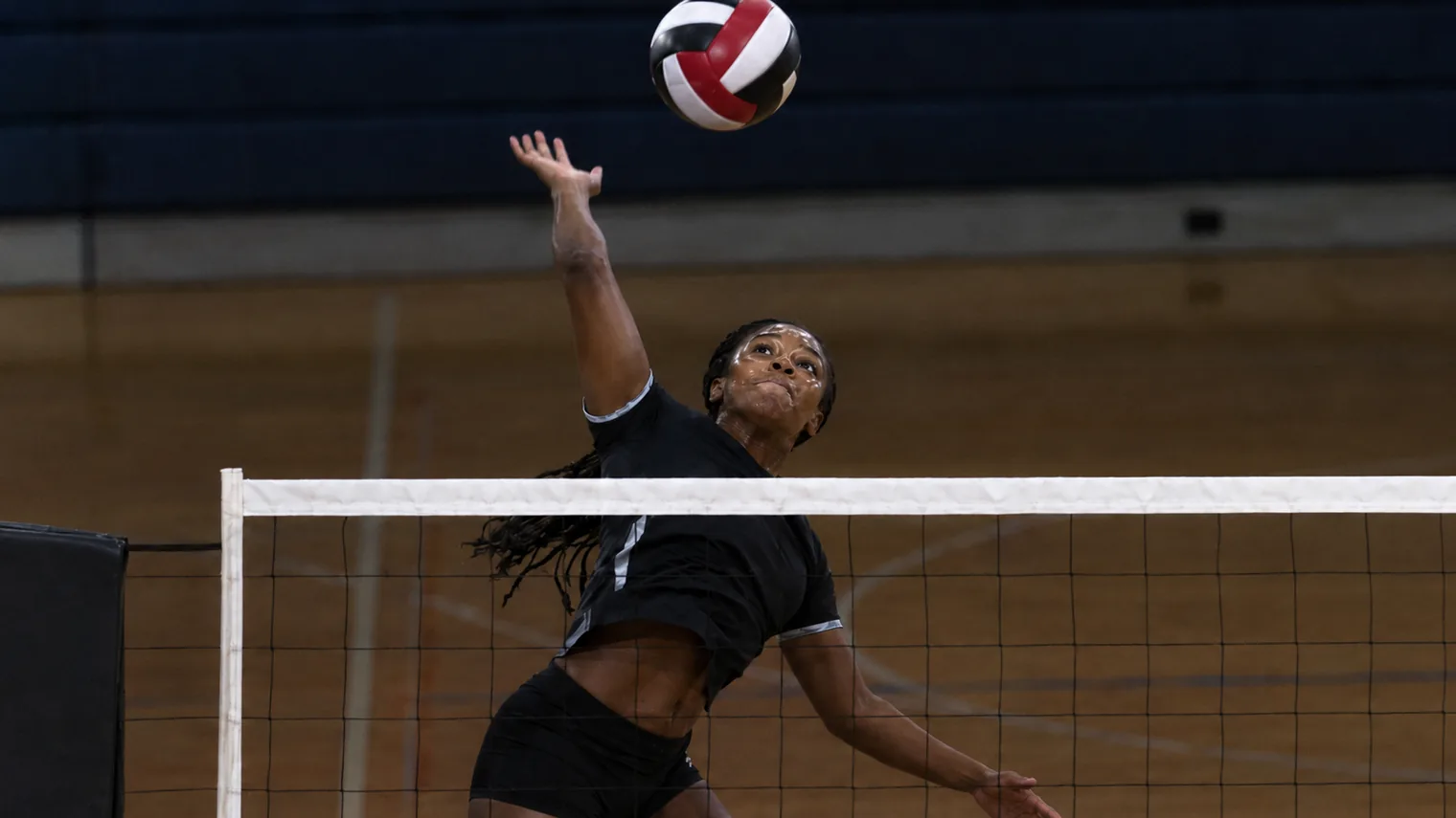 A volleyball player at the peak of a spike at the net in a dim gym