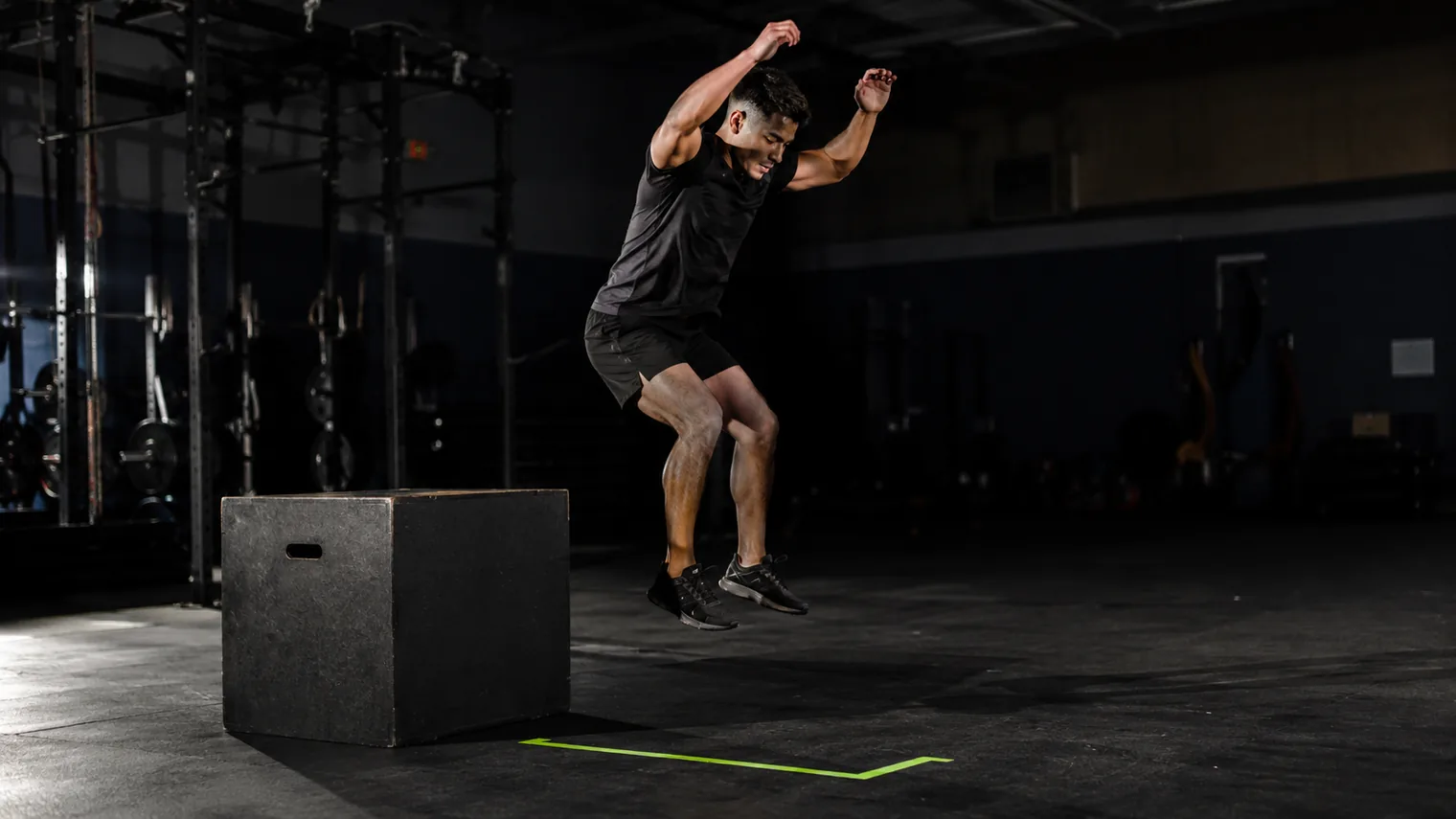 An athlete rebounding off a plyometric box during a depth jump in a gym
