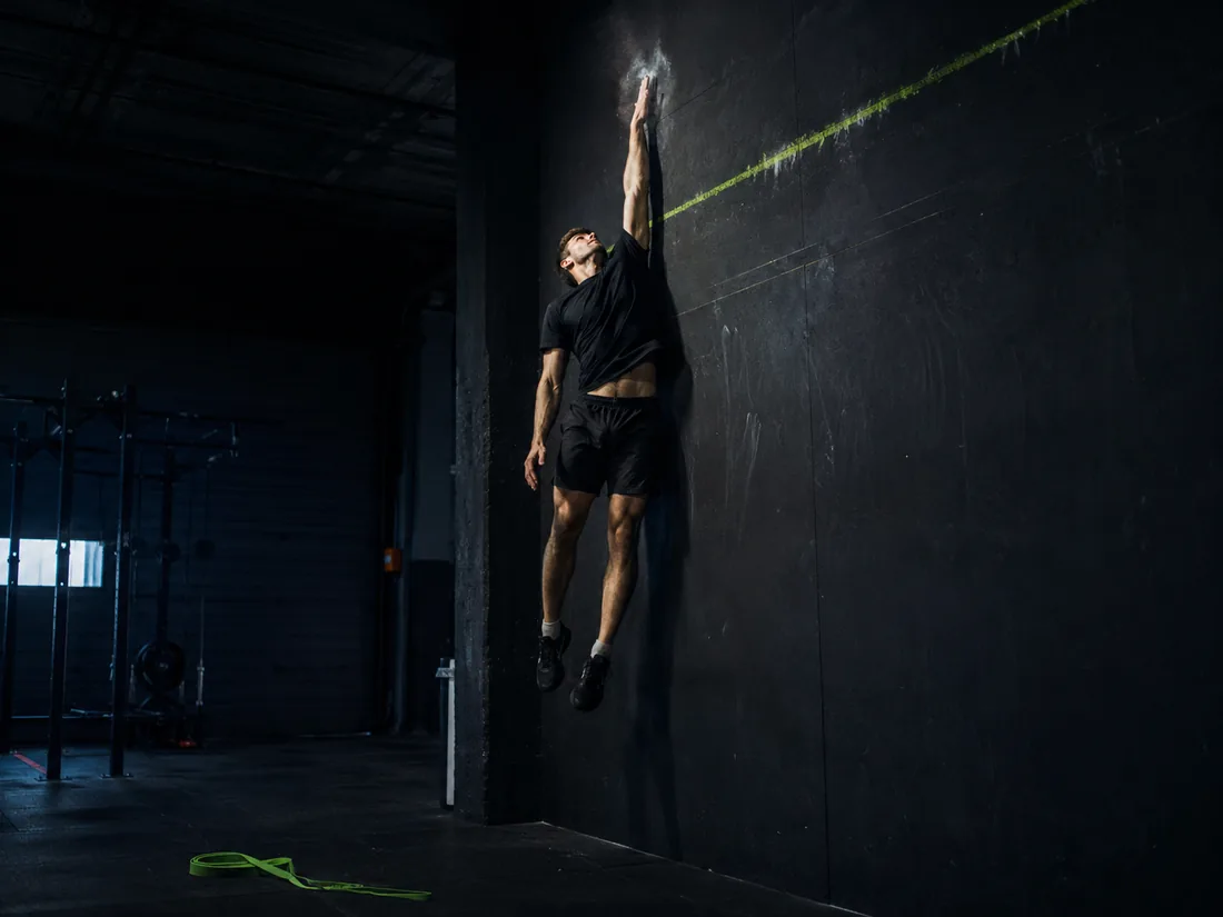 An athlete at the peak of a maximum vertical jump reaching for a chalk mark high on a wall